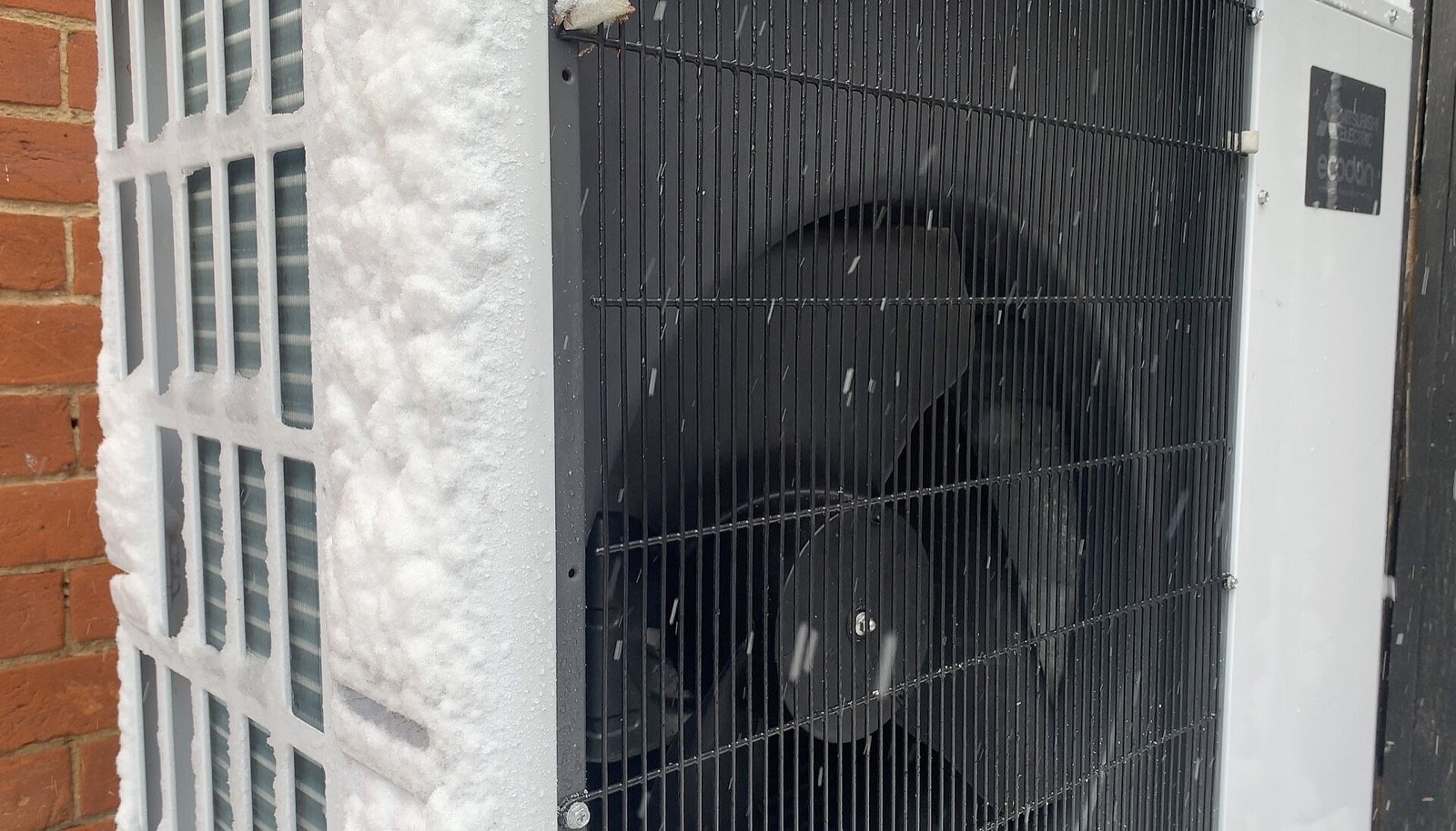 Wärmepumpe im Schneefall direkt an einer Backsteinwand